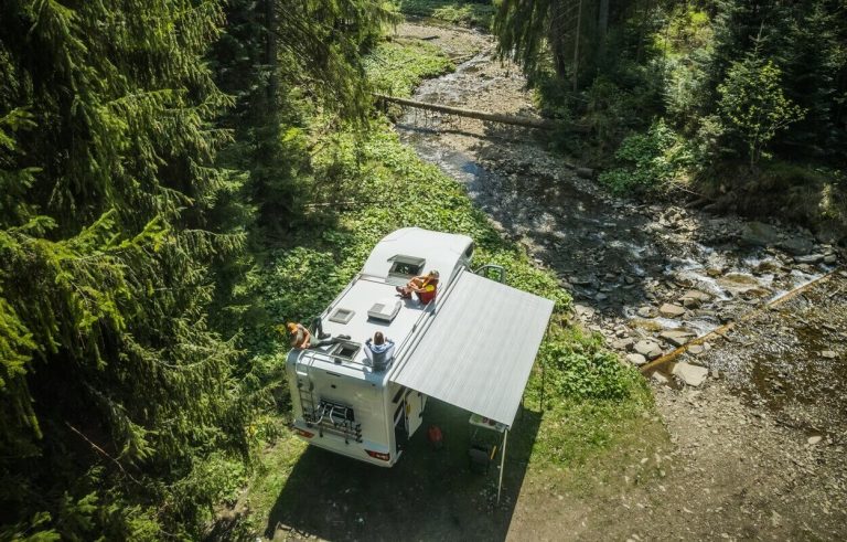 Caravana estacionada en el bosque con gente sobre el tejado